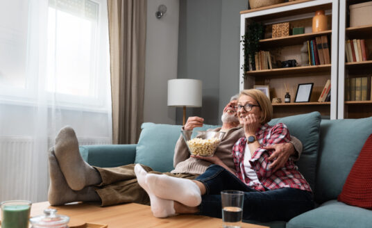 Old retired age couple watching TV at home, old mature couple cheering sport games competition together with laugh smile victory on sofa couch at living room home.