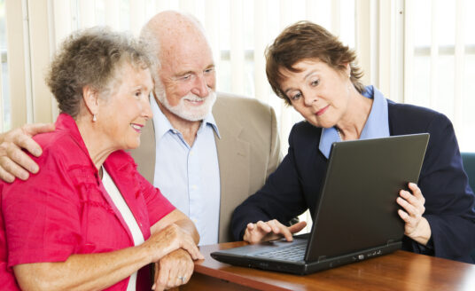 Senior man and woman talking to a younger woman while reviewing information on a laptop
