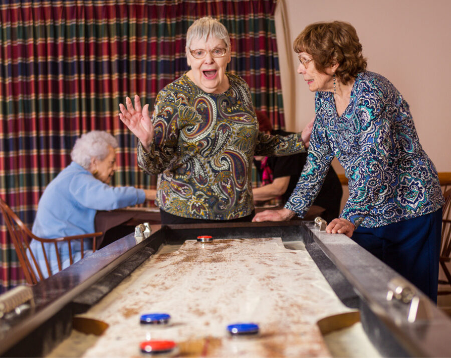Two senior women enjoy a game of shuffleboard in the game room at Village North