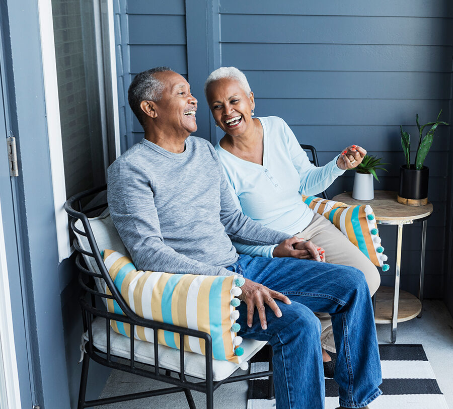 Senior man and woman chat and laugh on a porch chair