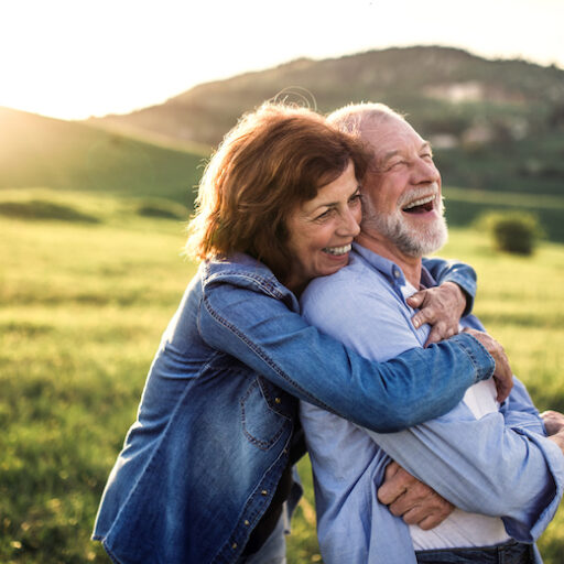 Side view of senior couple who live life to the fullest hugging outside in spring nature at sunset.