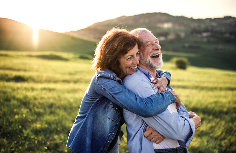 Side view of senior couple who live life to the fullest hugging outside in spring nature at sunset.