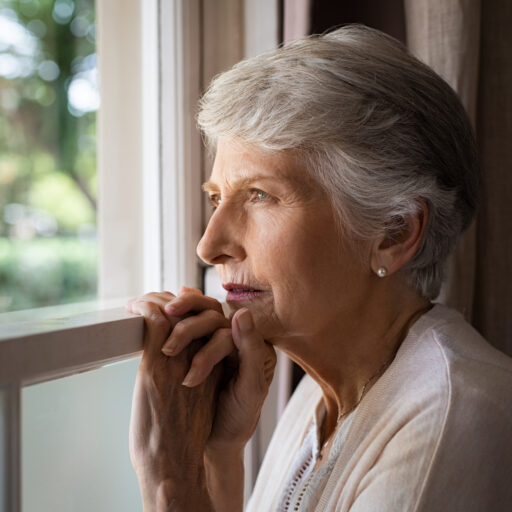 A senior woman, who is experiencing signs of depression, looks out the window.