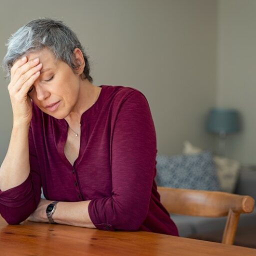 An older adult woman holds her head in her hand, a sign that she is stressed over her role as family caregiver, and may need to choose respite care.