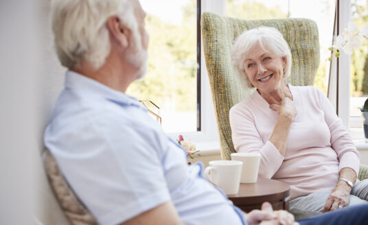 A senior couple living in a retirement community sits and chats in their personal apartment.