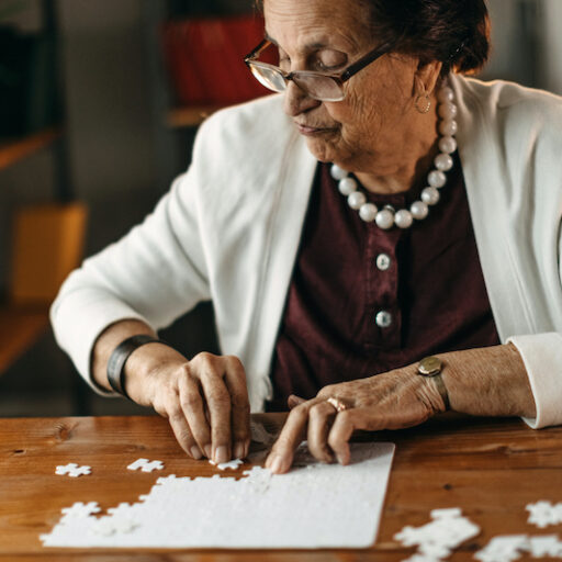 Senior woman putting together a puzzle on a wooden table, which is a great activity for seniors with dementia