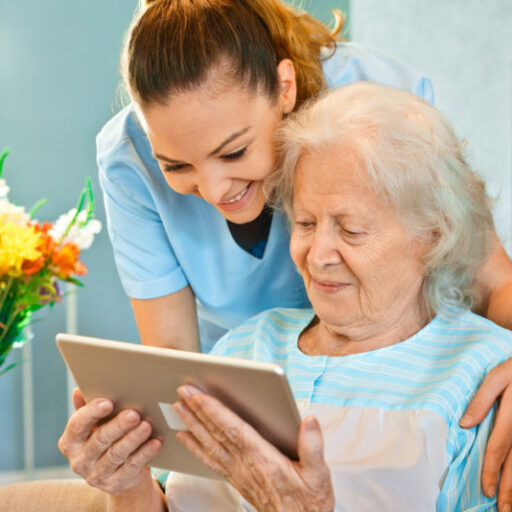 Respite care worker helps elderly woman use a tablet.