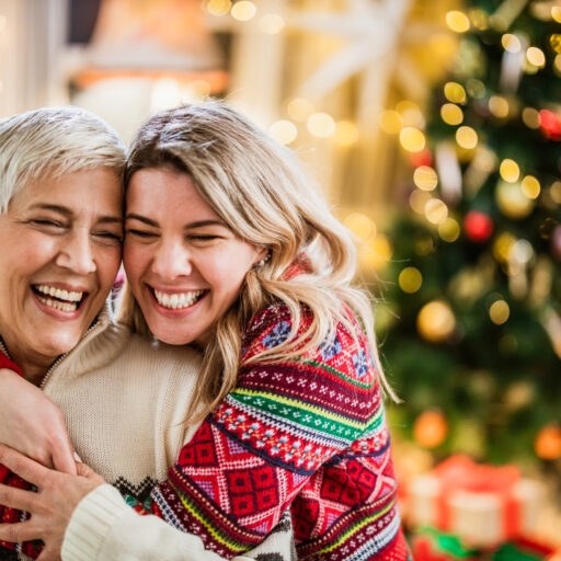 Young woman and senior woman celebrate the holidays by hugging in front of a decorated tree