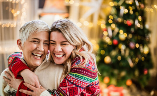 Young woman and senior woman celebrate the holidays by hugging in front of a decorated tree