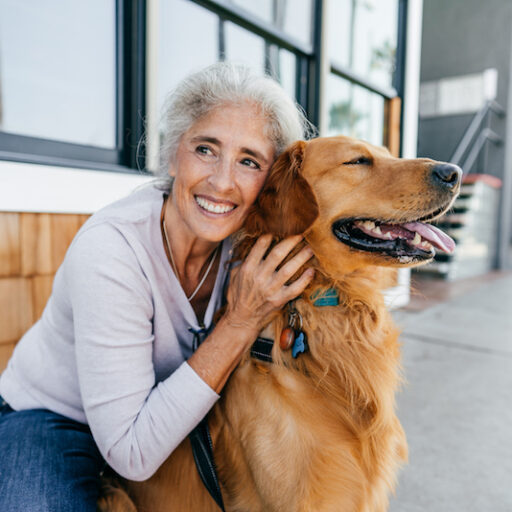A senior woman hugs her golden retriever on a porch