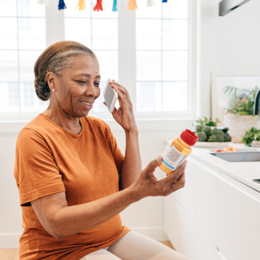 Senior woman on the phone looking at a prescription medication, practicing proper medication safety for seniors