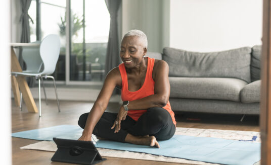 A senior woman practices self-care by preparing to do a yoga routine for optimal wellness for seniors.