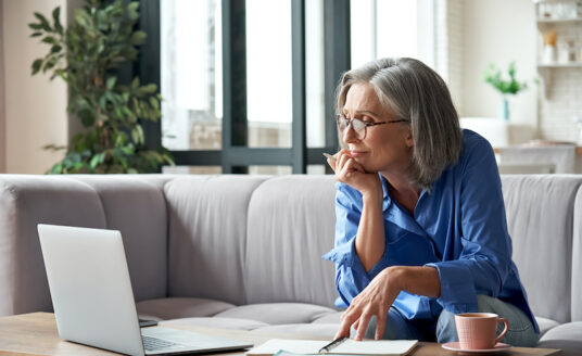 A senior woman seated on her couch in the living room, continuing education through an online course on her laptop