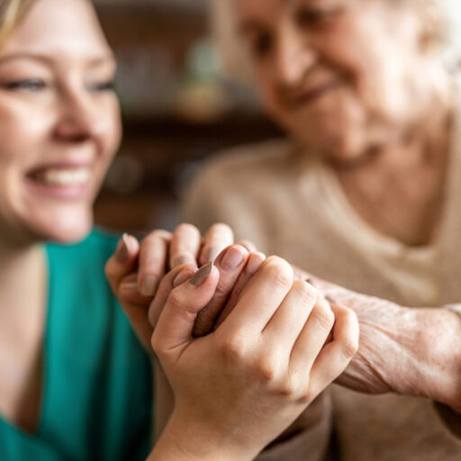 A young woman and older woman hold hands and smile in a hospice care facility, despite hospice care myths they may have heard.