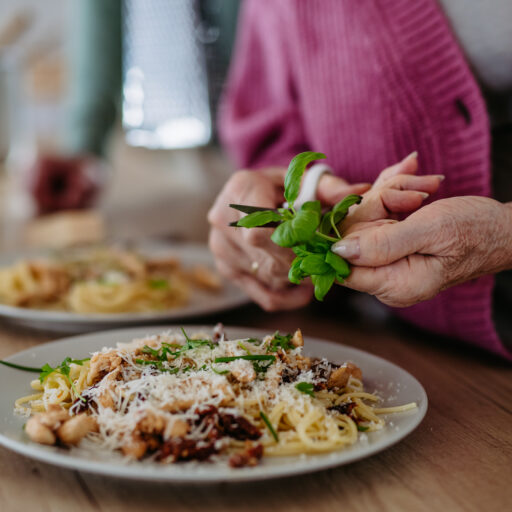 Senior woman snipping basil leaves from herb garden onto pasta