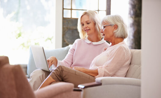 Adult daughter helping senior mother with computer in preparation for touring an assisted living community