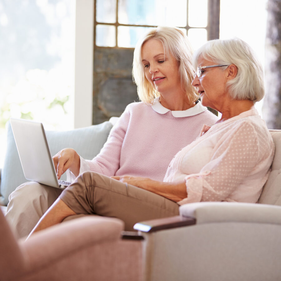 Adult daughter helping senior mother with computer in preparation for touring an assisted living community