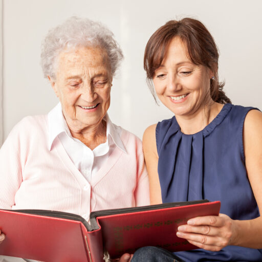 Woman demonstrating important dementia caregiver tips, looking through a photo album with senior woman