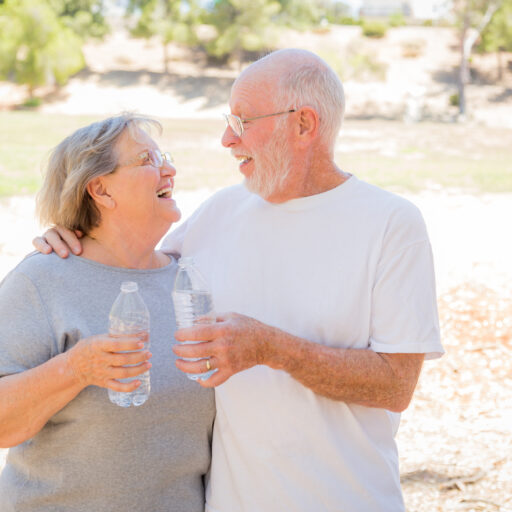 A senior couple focusing on hydration for seniors in the summer, with their water bottles in-hand.