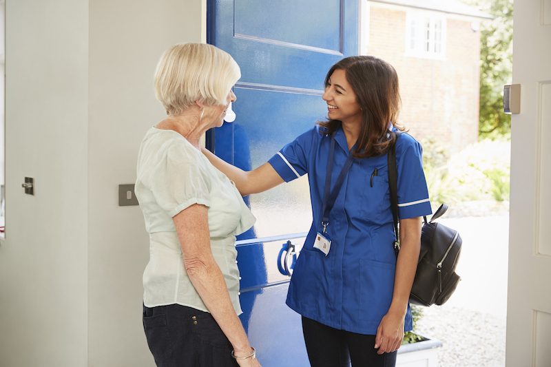 A nurse greets a senior woman at her door, as she arrives to provide home care for the senior.