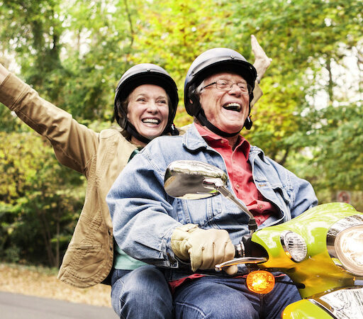 A happy senior couple riding a scooter as a way to enjoy fall activities for seniors