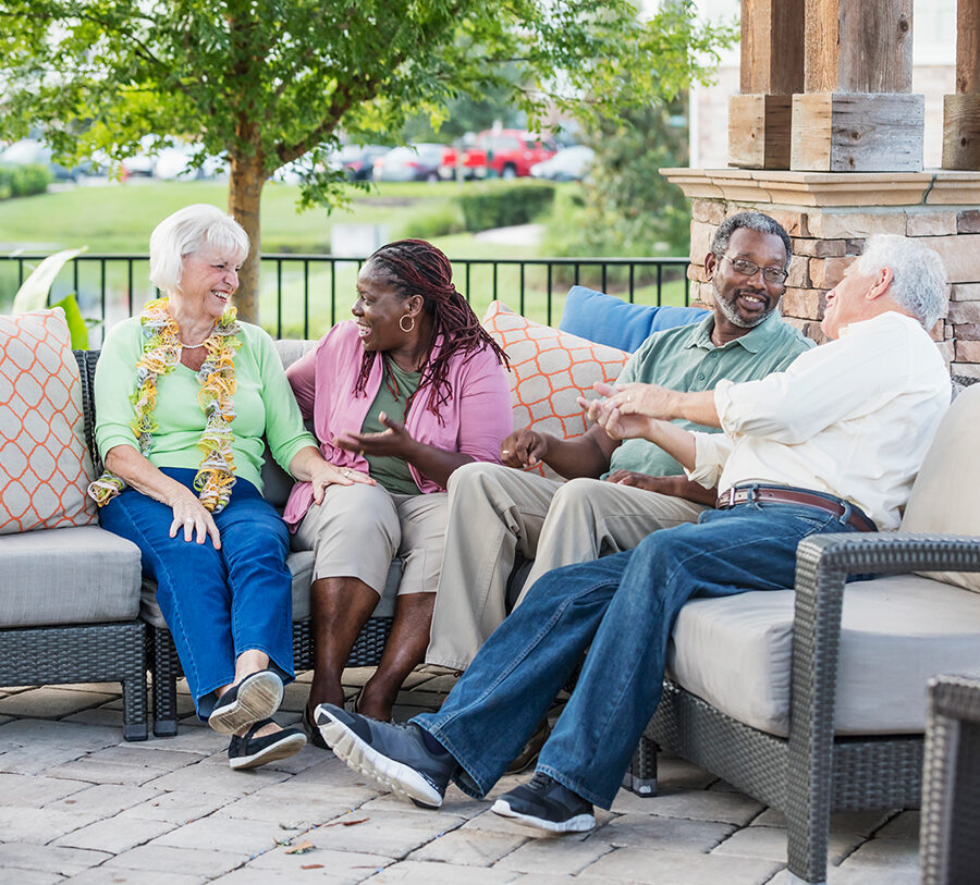 Two senior men and two senior women socialize outdoors on nice patio furniture
