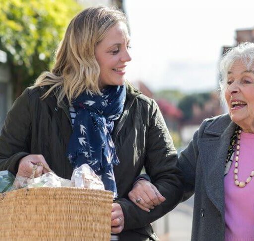 An adult woman carries groceries for a senior woman, as she knows that kindness makes you healther.